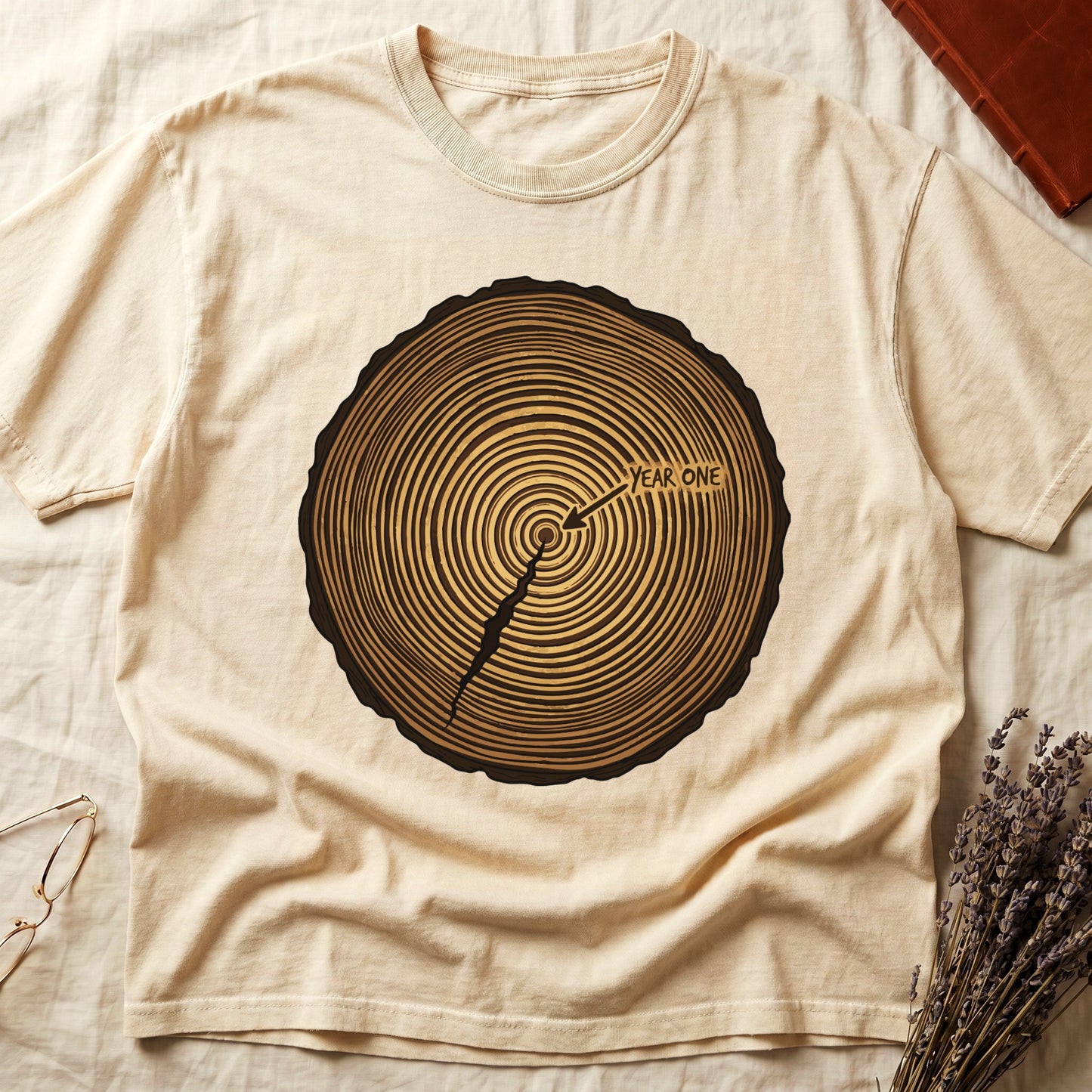 Ivory tee with cross-section of tree rings in warm brown, arrow pointing to center labeled "YEAR ONE" in serif type.