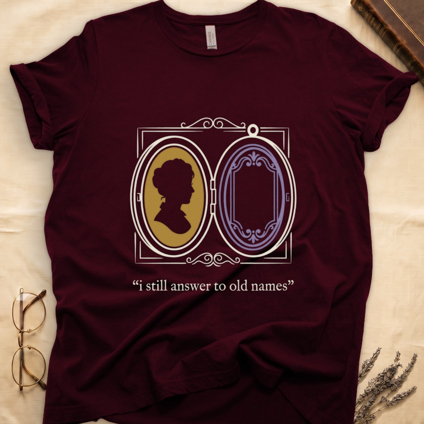 Maroon tee with Victorian double-locket, silhouette portrait in gold frame, "i still answer to old names" cream serif below.