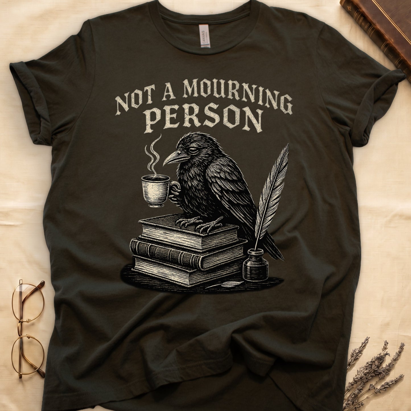Maroon tee with raven holding coffee on stack of books, quill in inkwell, "NOT A MOURNING PERSON" distressed serif top.