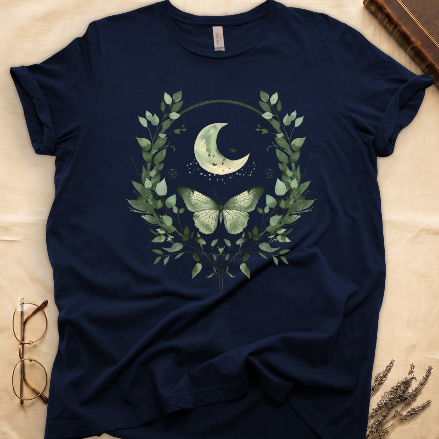 Navy t-shirt with crescent moon, butterfly, and green leaf wreath graphic.