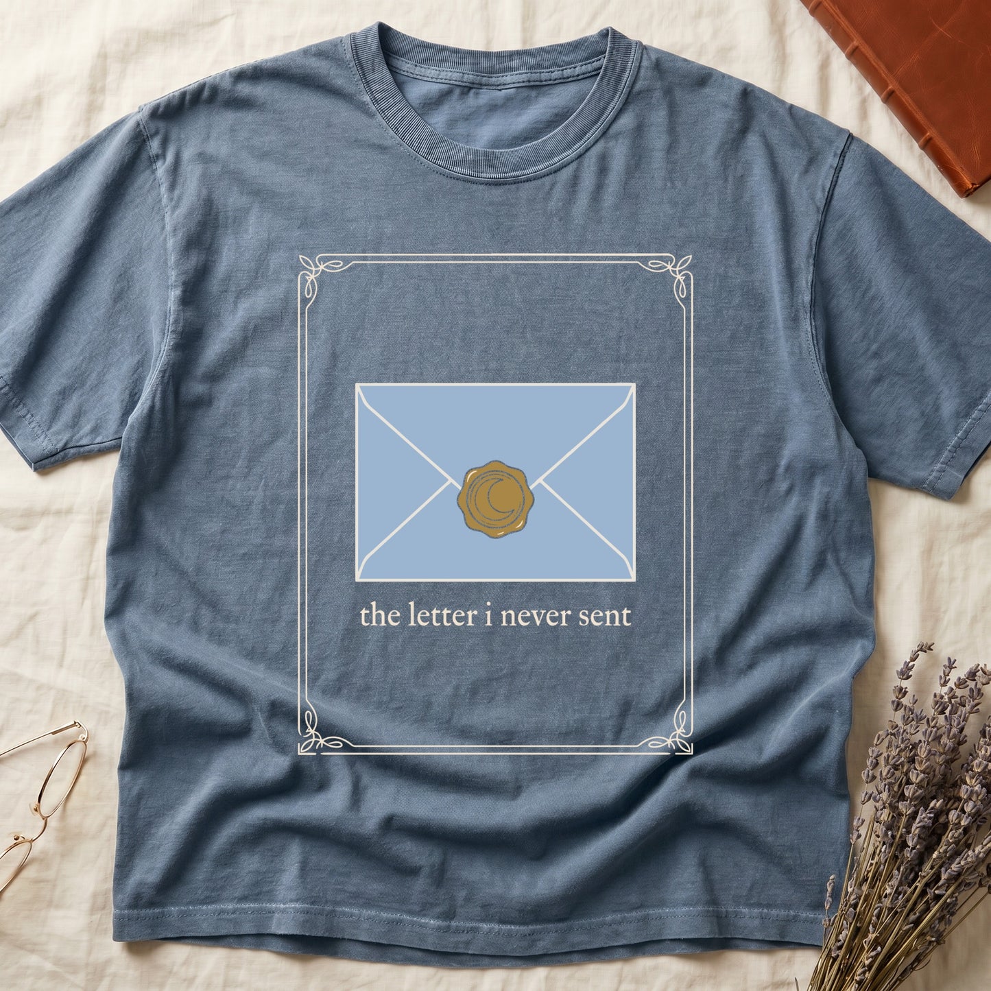 Blue Jean tee with pale blue envelope sealed with gold crescent moon wax seal, "the letter i never sent" cream serif below.