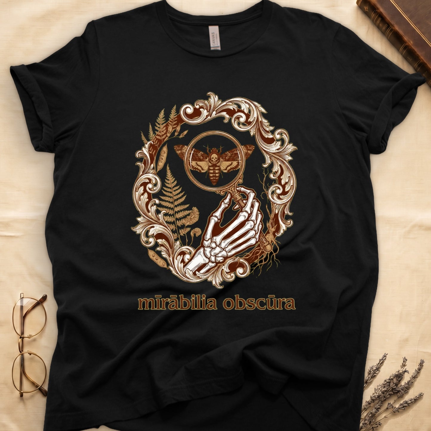 Black tee with skeletal hand, magnifying glass, death's-head moth, ferns on green, "mīrābilia obscūra" in Latin italic.