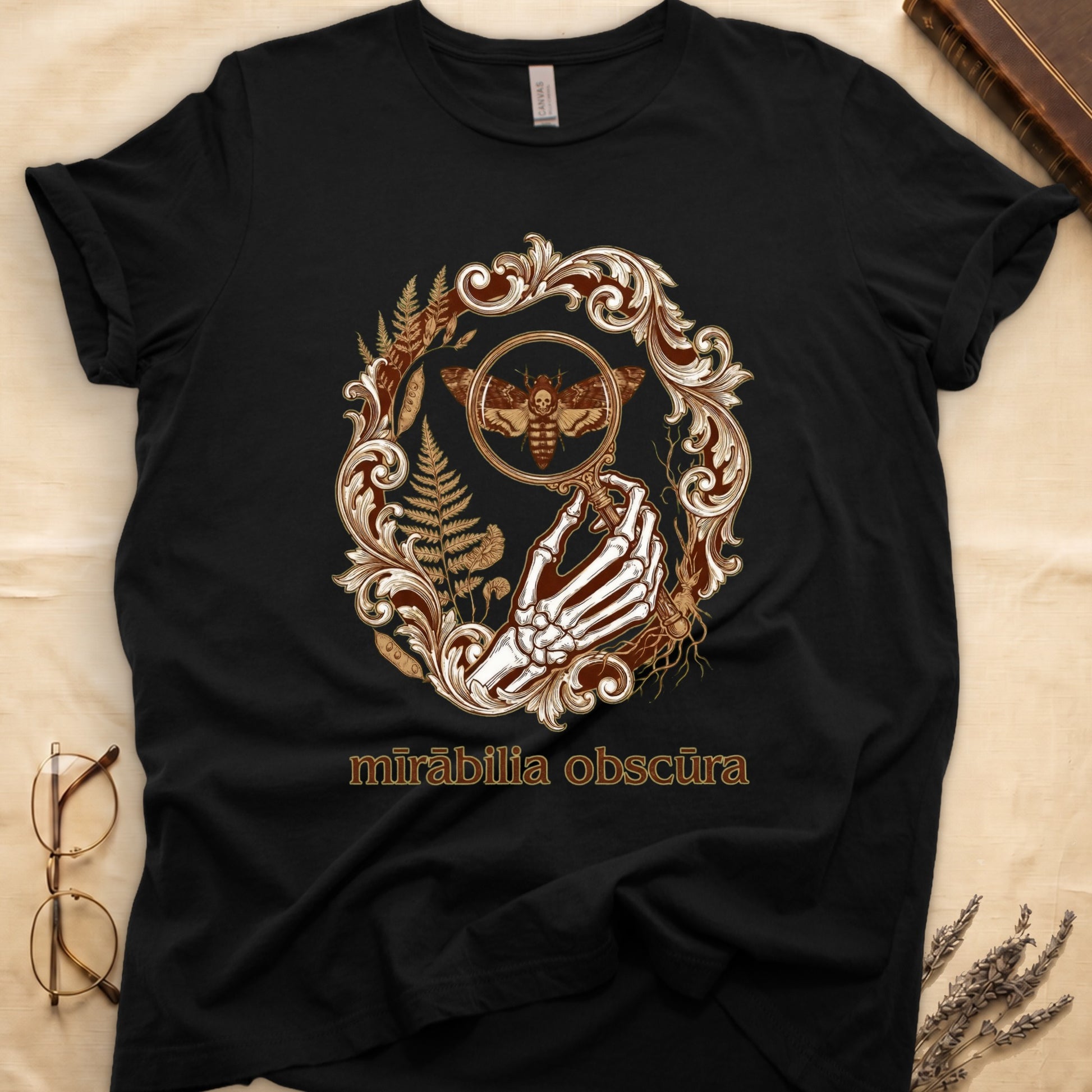 Black tee with skeletal hand, magnifying glass, death's-head moth, ferns on green, "mīrābilia obscūra" in Latin italic.
