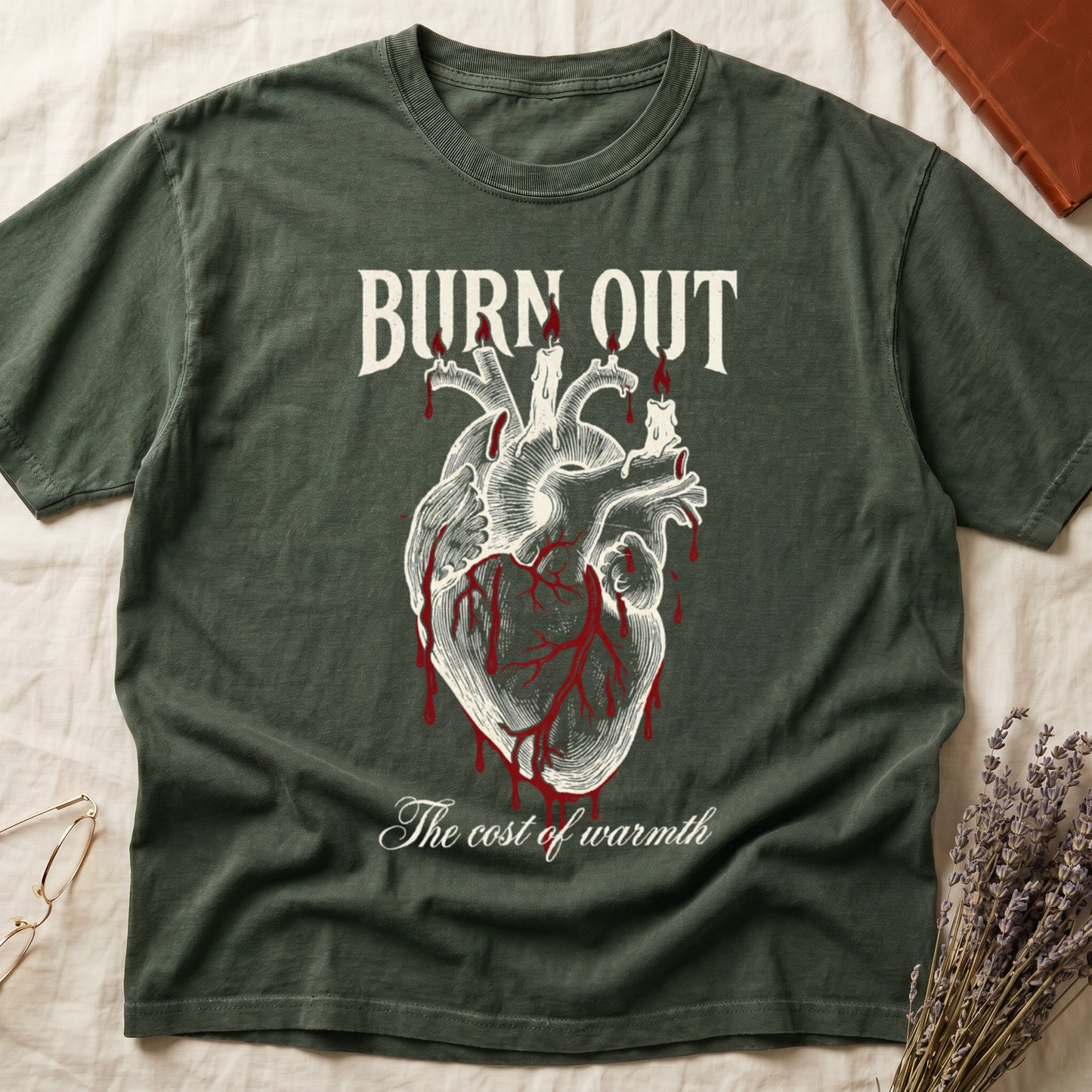 Green tee with anatomical heart and melted candles dripping red wax, "BURN OUT" top, "The cost of warmth" cursive below.