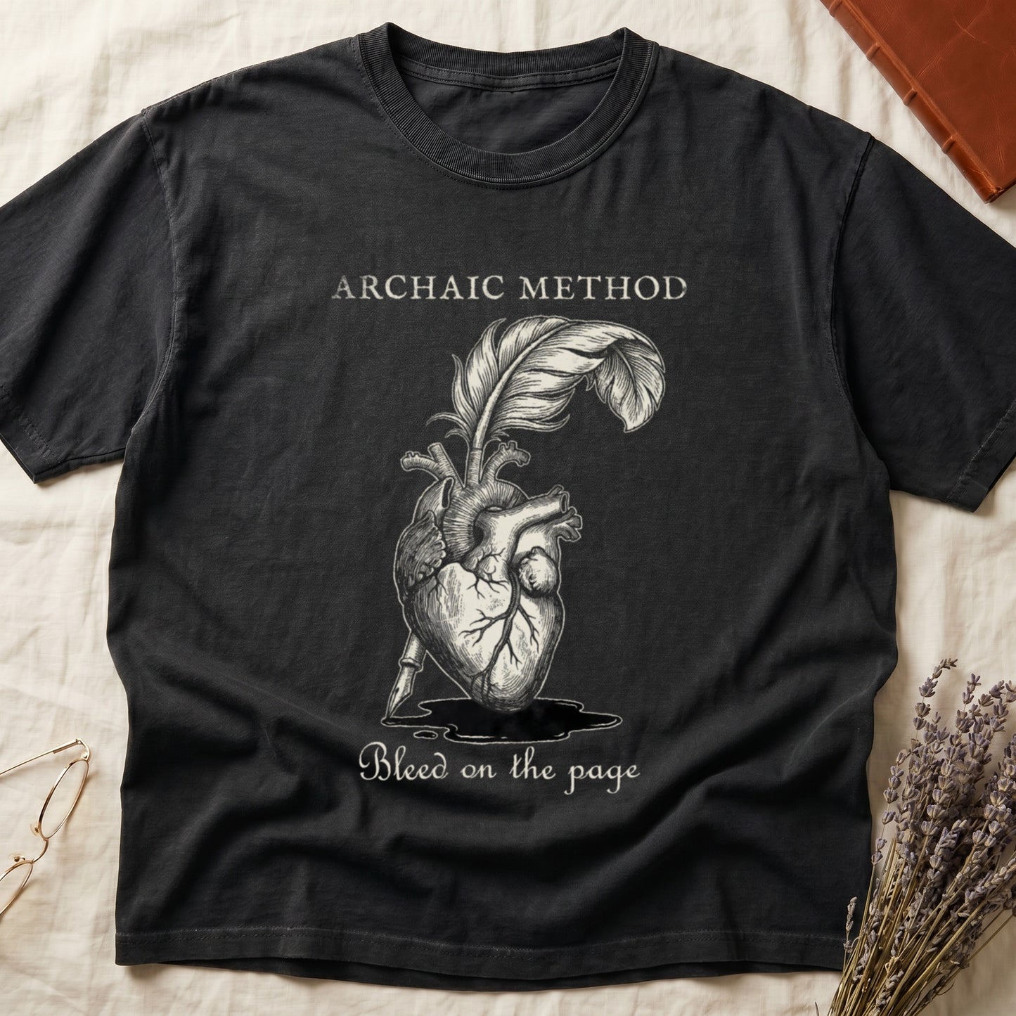 Black tee with anatomical heart and quill emerging in cream linework, "ARCHAIC METHOD" top, "Bleed on the page" below.
