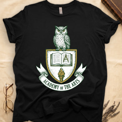 Black tee with heraldic shield crest, owl perched on top, open book and dividers center, "ACADEMY OF THE ARTS" on a banner.