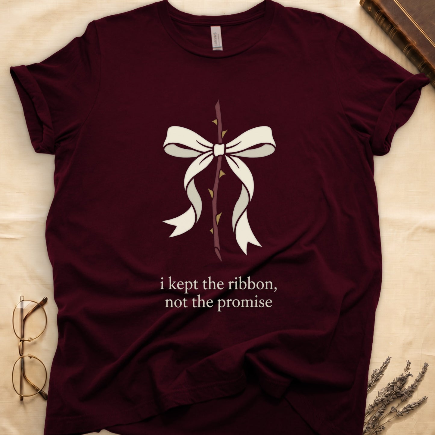 Maroon tee with cream bow tied around thorny rose stem, "i kept the ribbon, not the promise" in cream serif below.