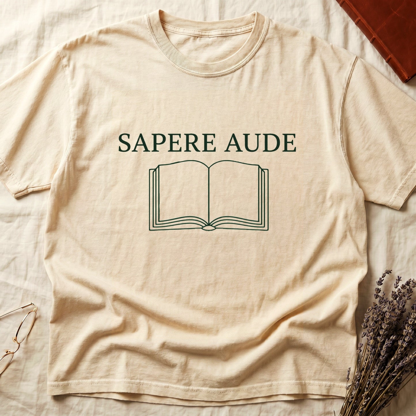 Ivory tee with "SAPERE AUDE" in serif capitals above a minimalist open book in cream linework.