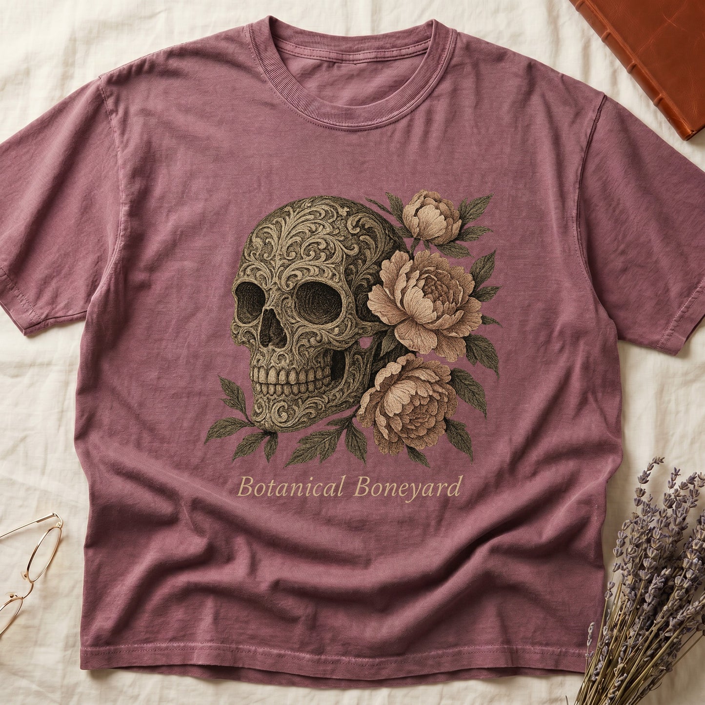 Dark Rose tee with filigree-engraved skull on left, peach-cream peonies on right, crossed bones below, "Botanical Boneyard."