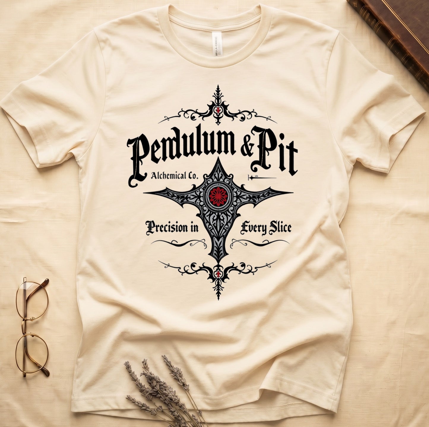 Natural tee with white talismanic cross, "Pendulum & Pit Alchemical Co.," "Precision in Every Slice" banner ribbons.