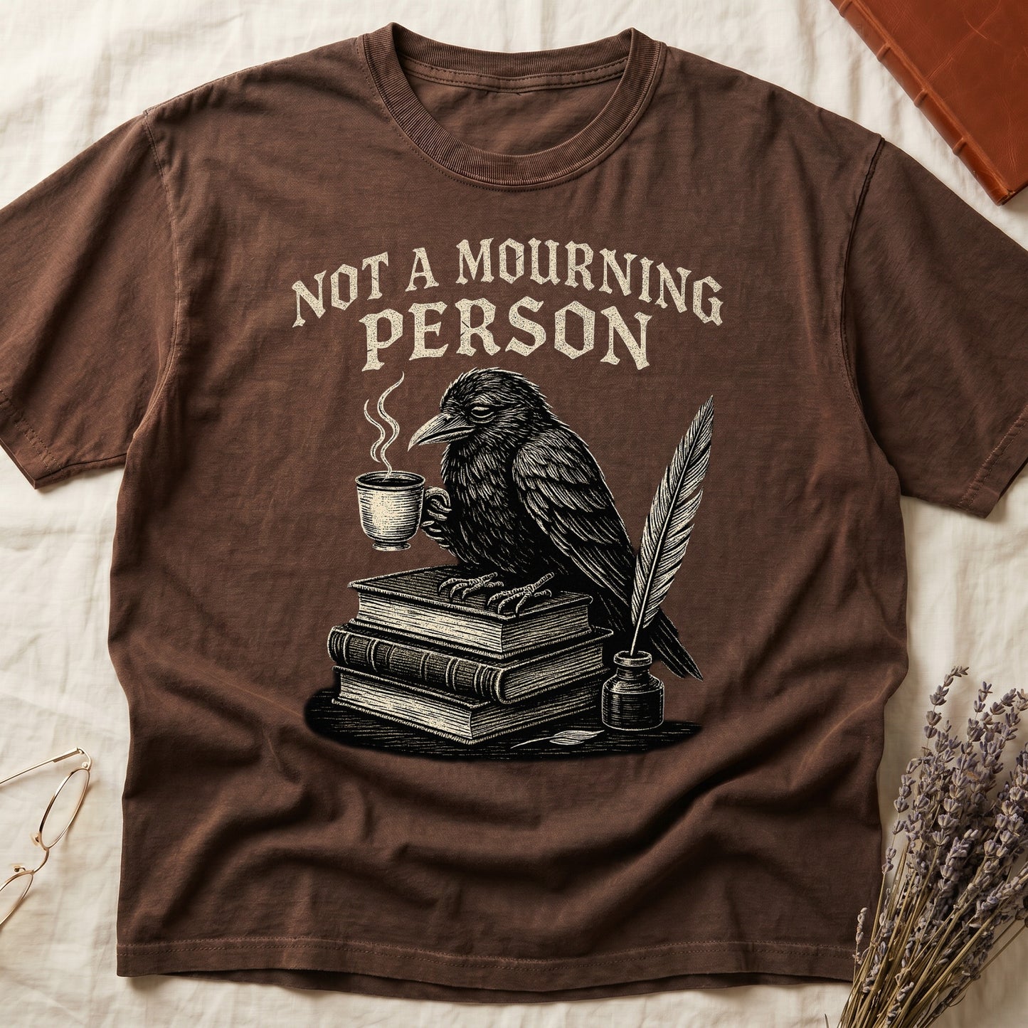 Black tee with raven holding coffee on stack of books, quill in inkwell, "NOT A MOURNING PERSON" distressed serif top.