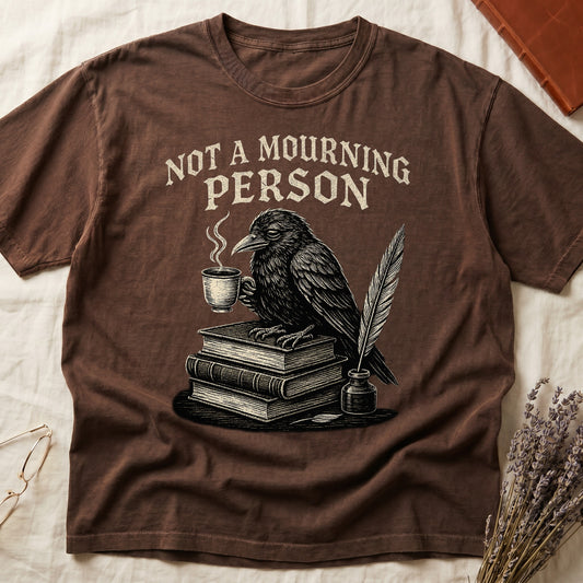 Black tee with raven holding coffee on stack of books, quill in inkwell, "NOT A MOURNING PERSON" distressed serif top.