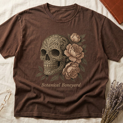 Espresso tee with filigree-engraved skull on left, peach-cream peonies on right, crossed bones below, "Botanical Boneyard."