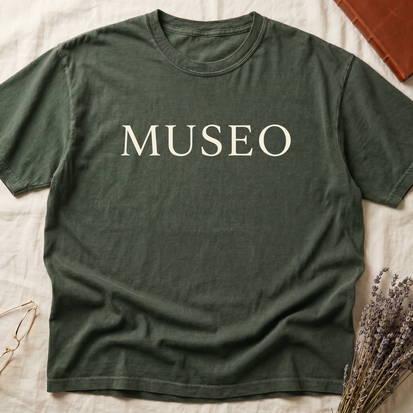 Green tee with "MUSEO" in oversized cream serif capitals, minimalist typographic design.