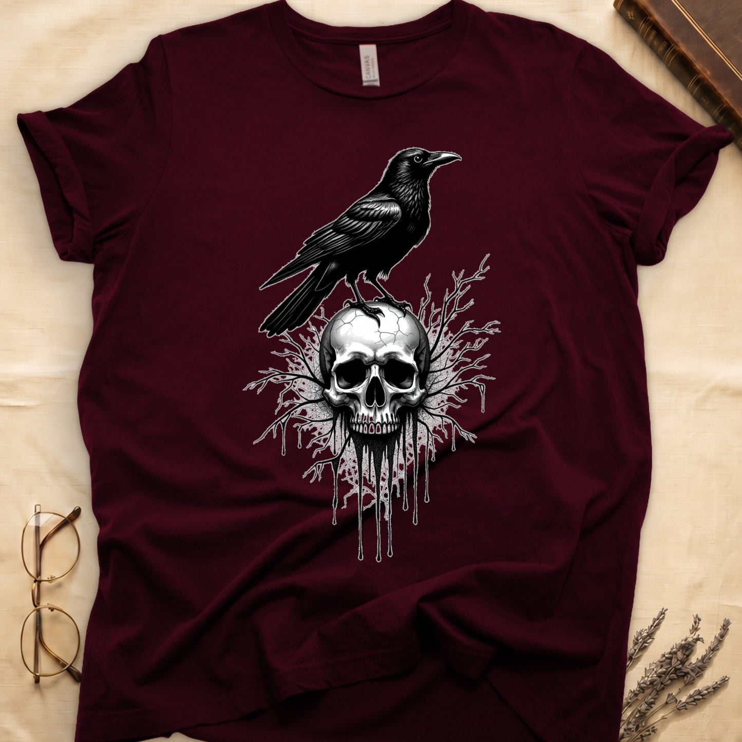 Maroon tee with raven silhouette on human skull, ink drips from jaw, bare branches behind, monochrome illustration.