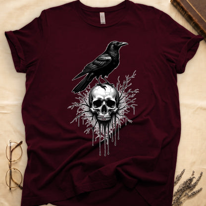Maroon tee with raven silhouette on human skull, ink drips from jaw, bare branches behind, monochrome illustration.