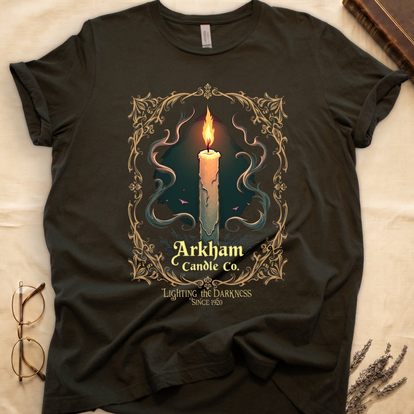Military Green tee with lit candle, smoke, ornate gold filigree border, "Arkham Candle Co.," "Lighting the Darkness Since 1920."