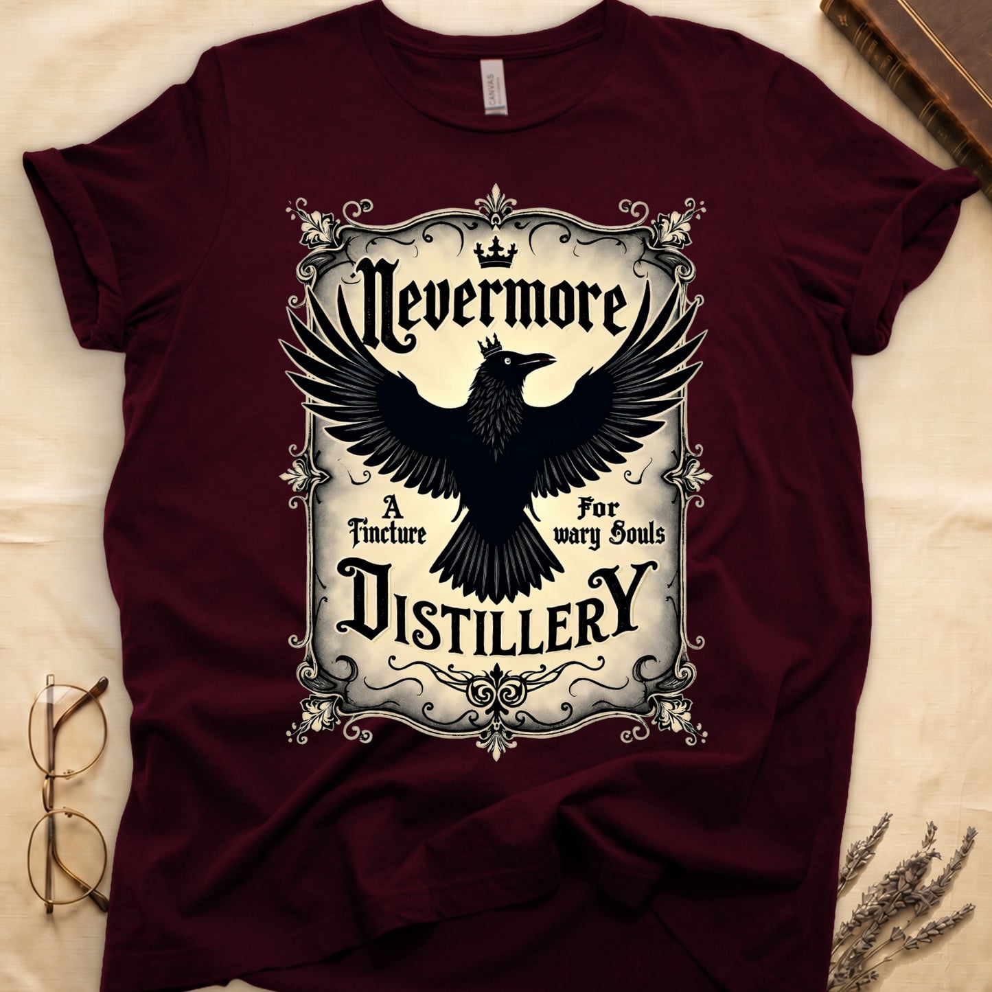 Maroon tee with antique label, crowned raven, blackletter "Nevermore" top, "A Tincture For wary Souls," "DISTILLERY" bottom.