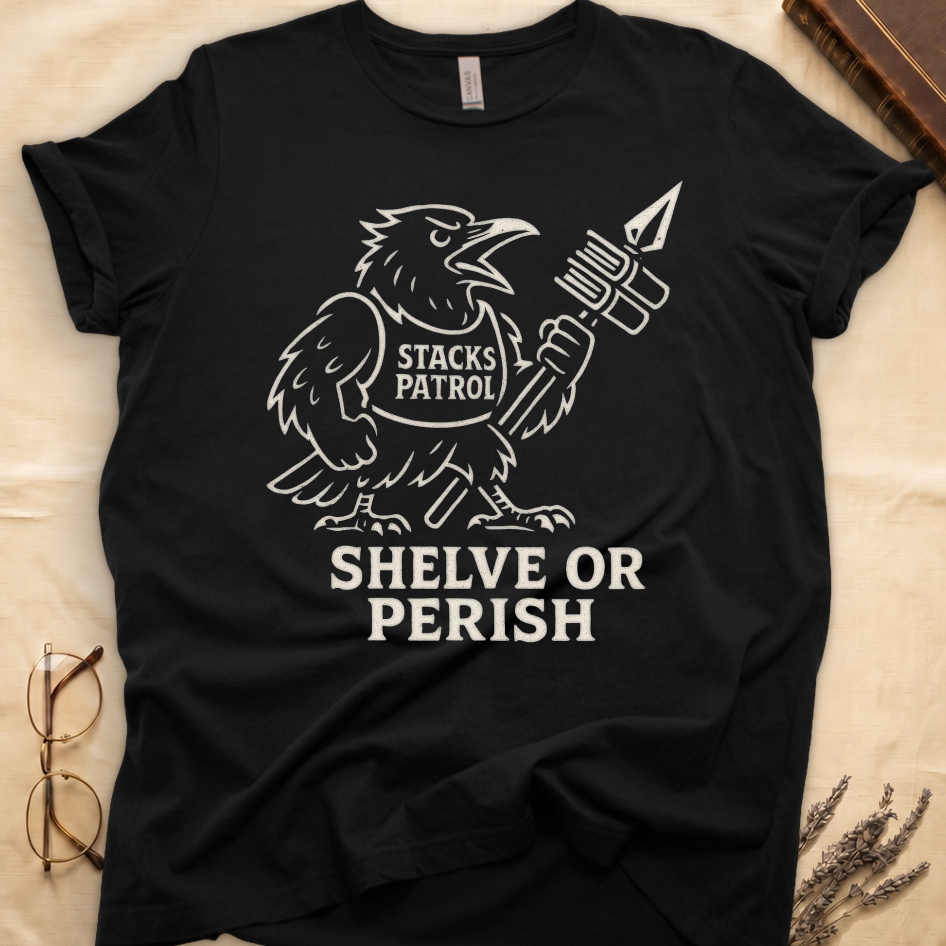 Black tee with vintage raven mascot, "STACKS PATROL" sash, feather pen aloft, "SHELVE OR PERISH" bold serif below.