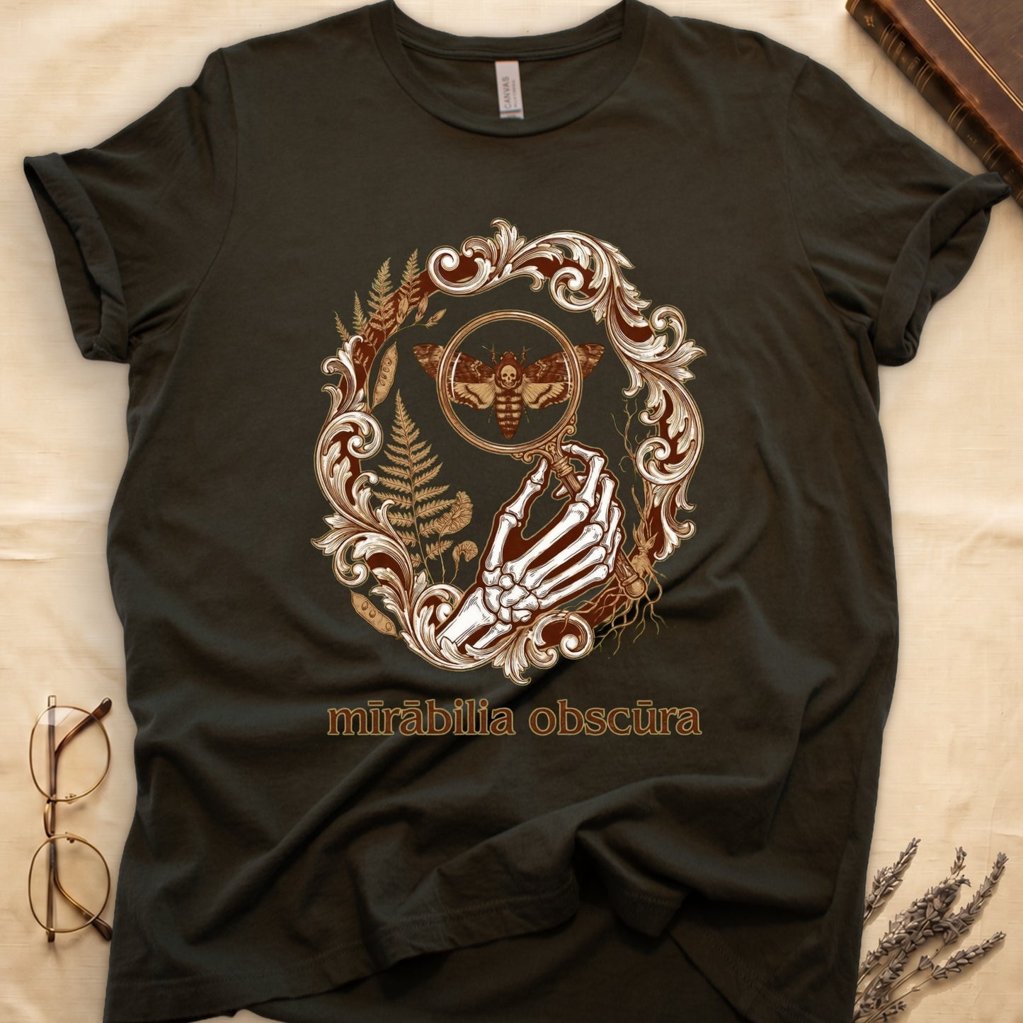 Military Green tee with skeletal hand, magnifying glass, death's-head moth, ferns on green, "mīrābilia obscūra" in Latin italic.