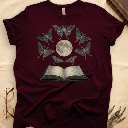 Maroon tee with full moon center, seven luna moths in halo around, open book below, cream-on-black engraving.