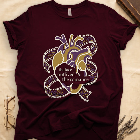 Maroon tee with anatomical heart in purple and gold wrapped in lace ribbons, "the lace outlived the romance" in serif.