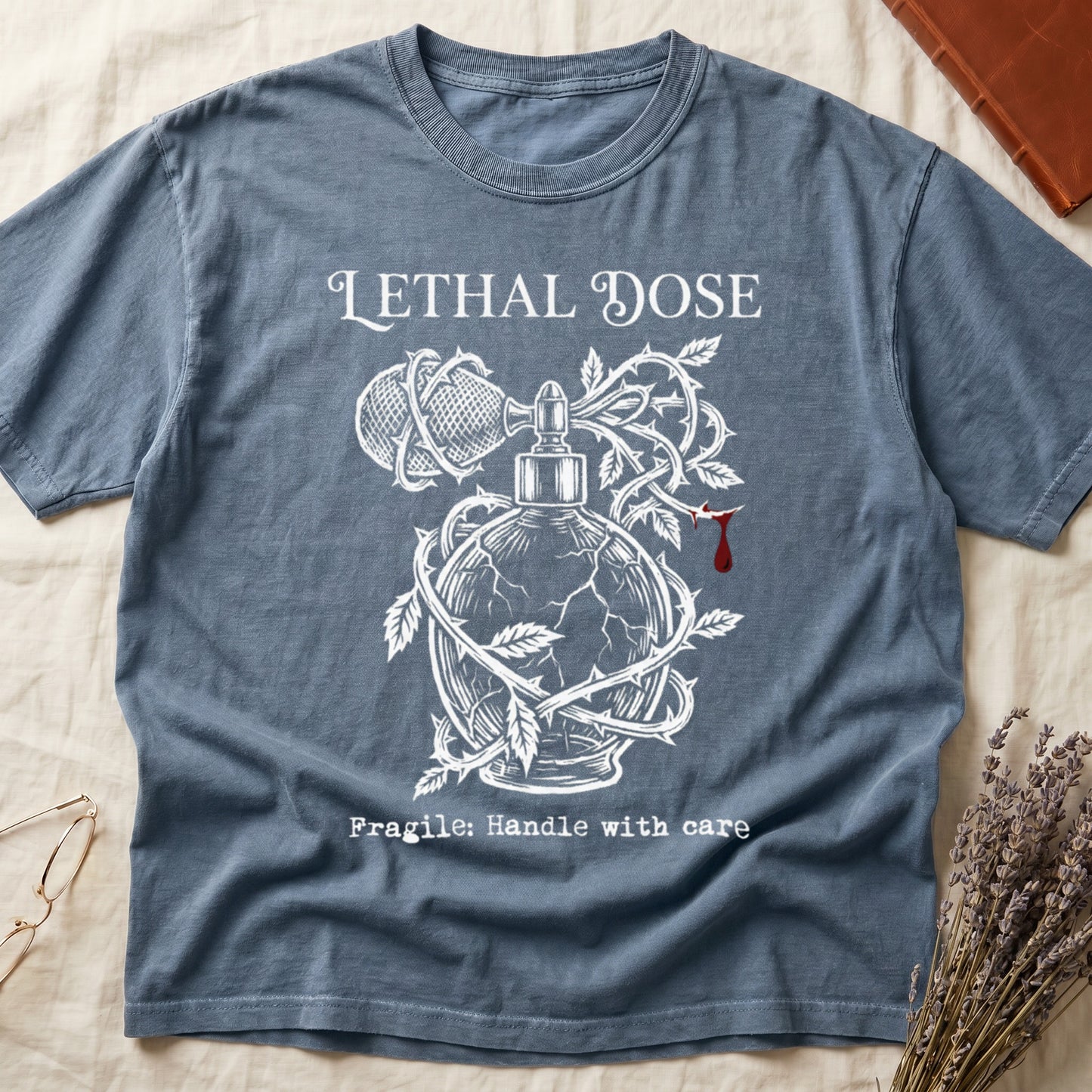 Blue Jean tee with cracked perfume bottle wrapped in thorns, blood drop, "LETHAL DOSE" top, "Fragile: Handle with care" below.