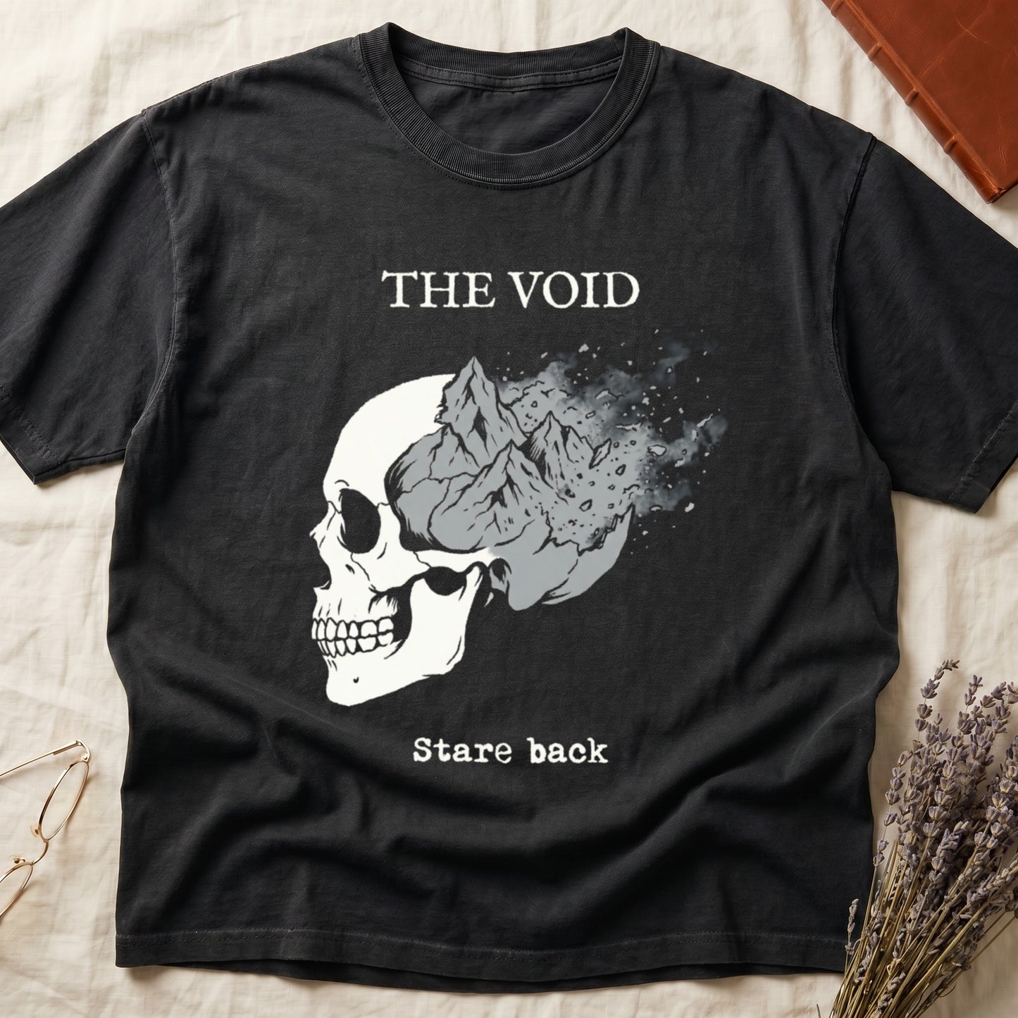 Black tee with skull eroding into mountain landscape and stardust, "THE VOID" top, "Stare back" typewriter below.