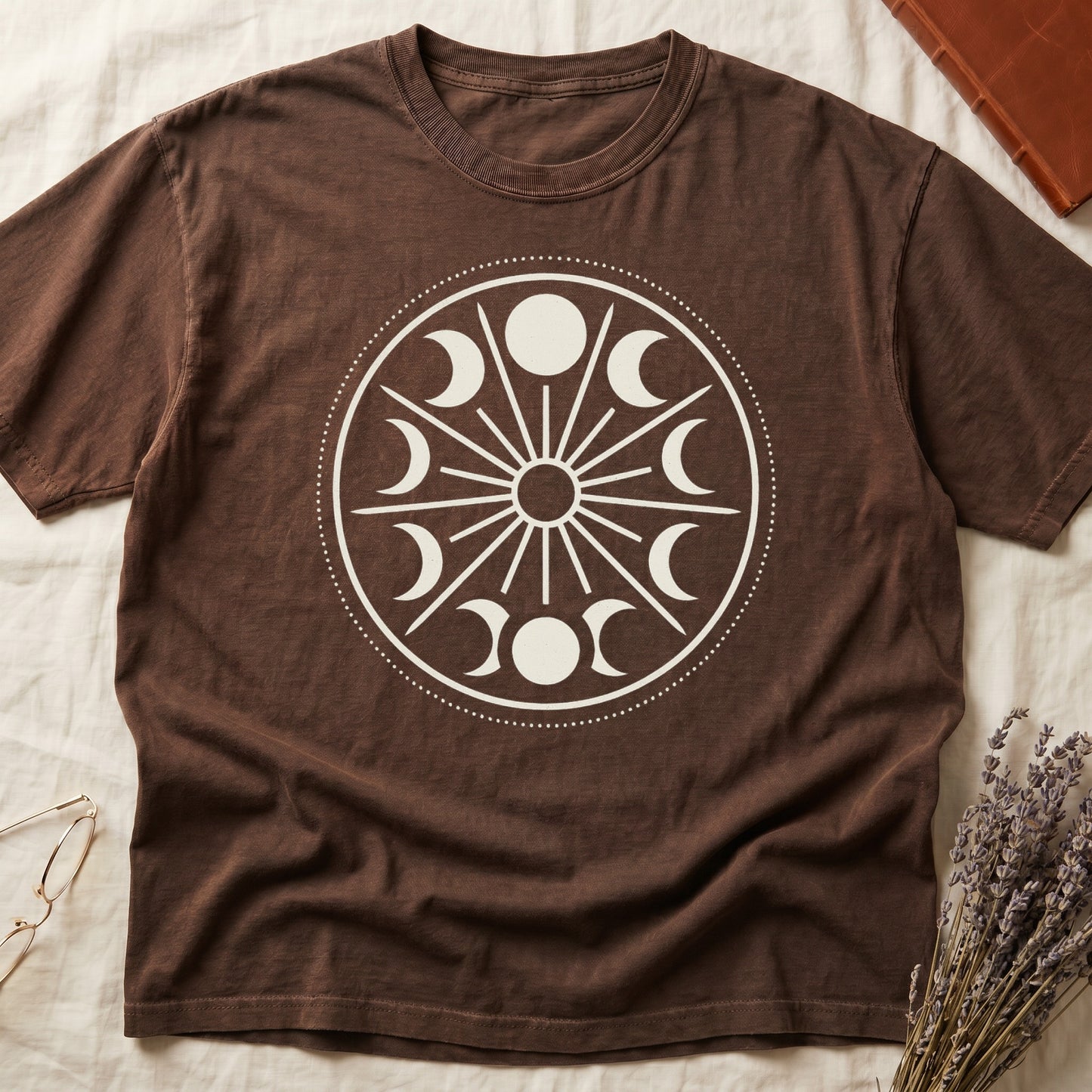 Espresso tee with cream lunar orrery wheel, dotted ring, radial sunburst, moon phases around perimeter, central star.