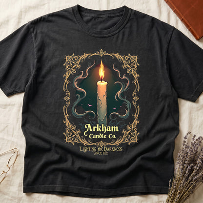 Black tee with lit candle, smoke, ornate gold filigree border, "Arkham Candle Co.," "Lighting the Darkness Since 1920."