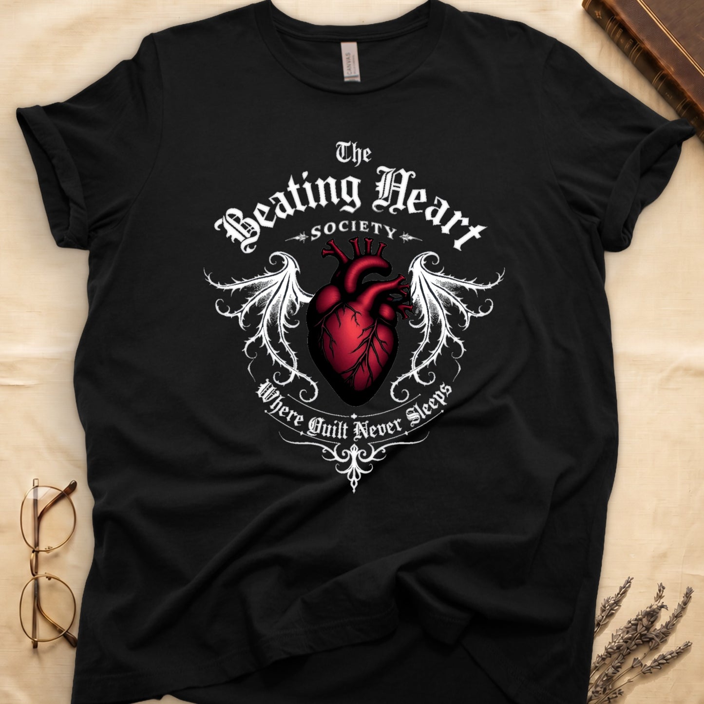 Black tee with anatomical red heart, gothic wings, "The Beating Heart SOCIETY," "Where Guilt Never Sleeps" below.