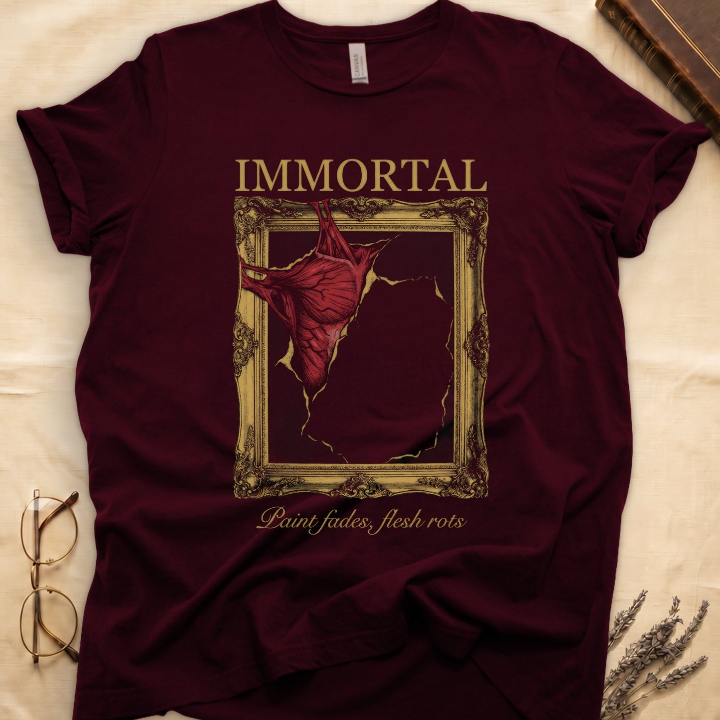 Maroon tee with gold frame and exposed muscle tearing canvas, "IMMORTAL" top, "Paint fades, flesh rots" italic below.