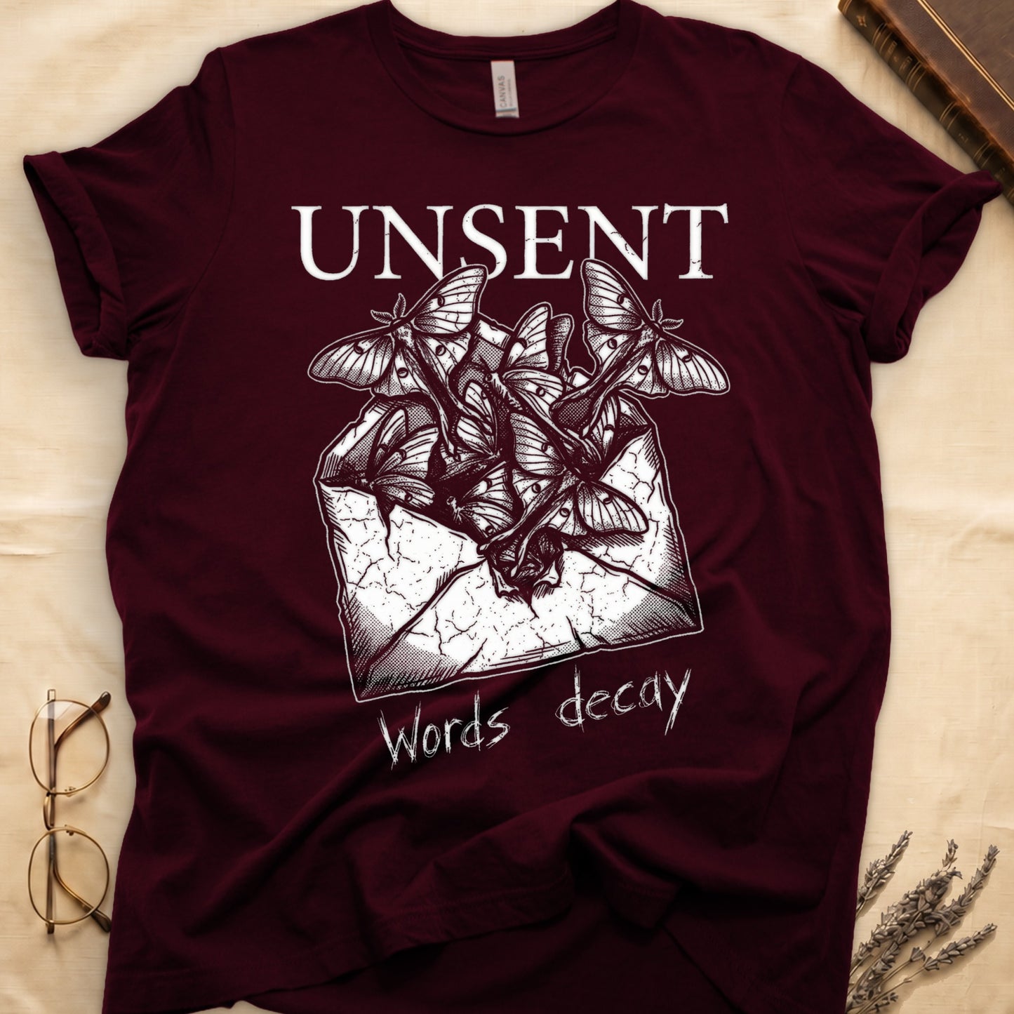 Maroon tee with 'UNSENT' in serif type, 'Words decay' brush text, luna moths from torn envelope in crosshatched ink