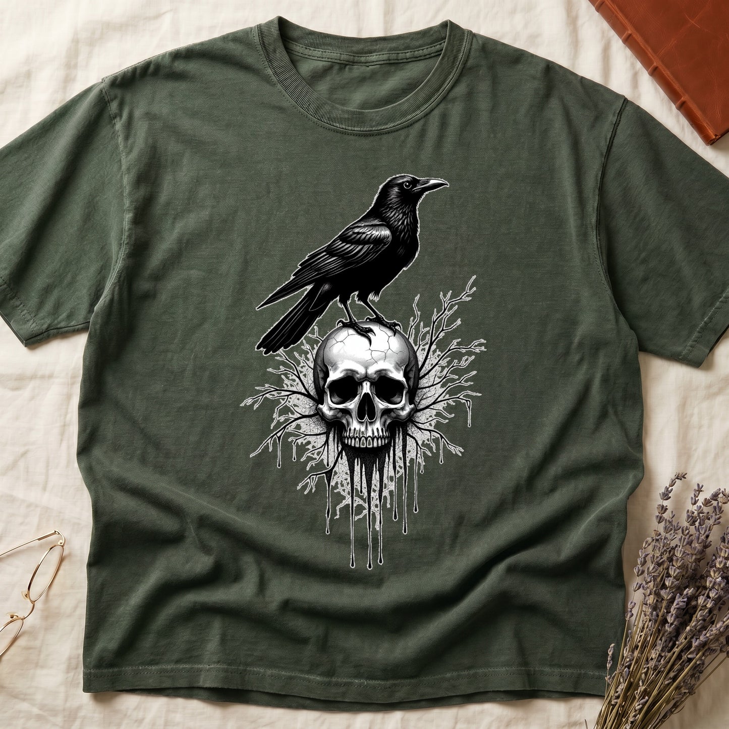 Green tee with raven silhouette on human skull, ink drips from jaw, bare branches behind, monochrome illustration.