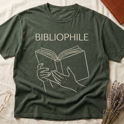 Green tee with two hands cradling an open book in cream and brown linework, "BIBLIOPHILE" in serif capitals above.