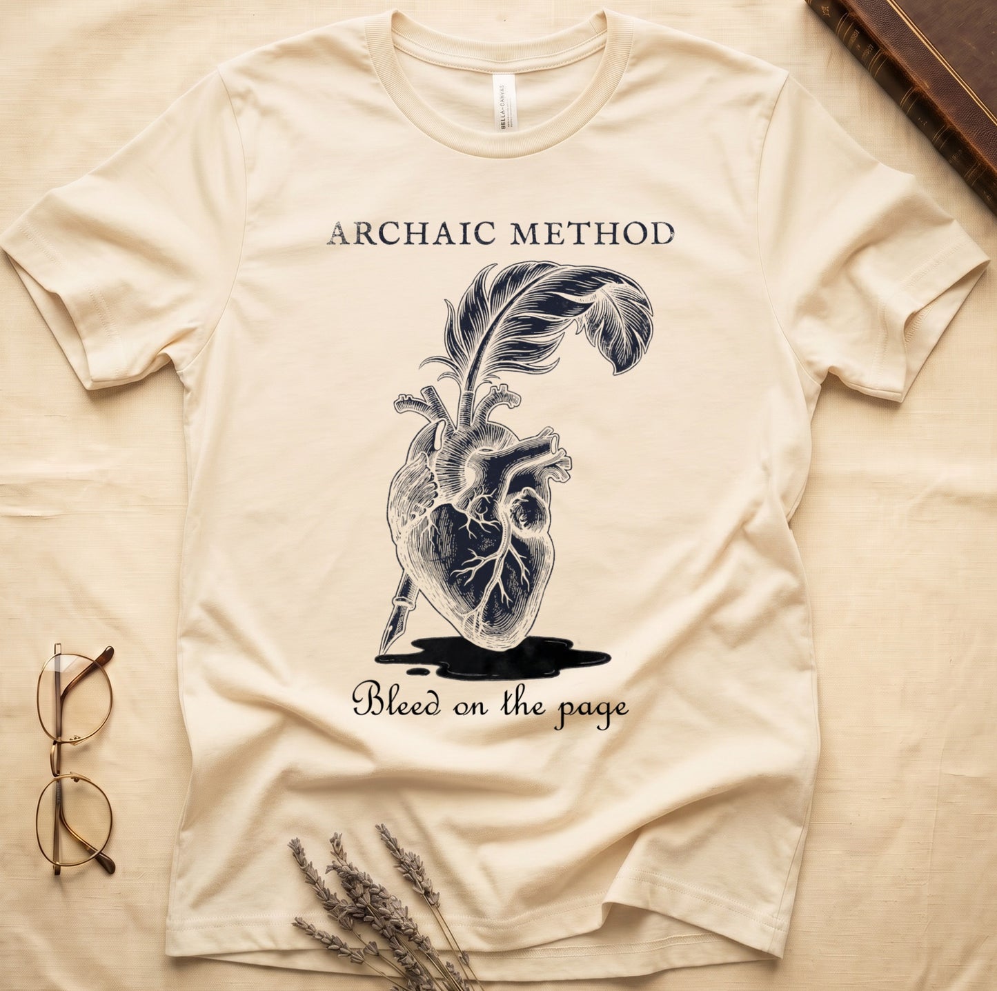 Natural tee with anatomical heart and quill emerging in cream linework, "ARCHAIC METHOD" top, "Bleed on the page" below.