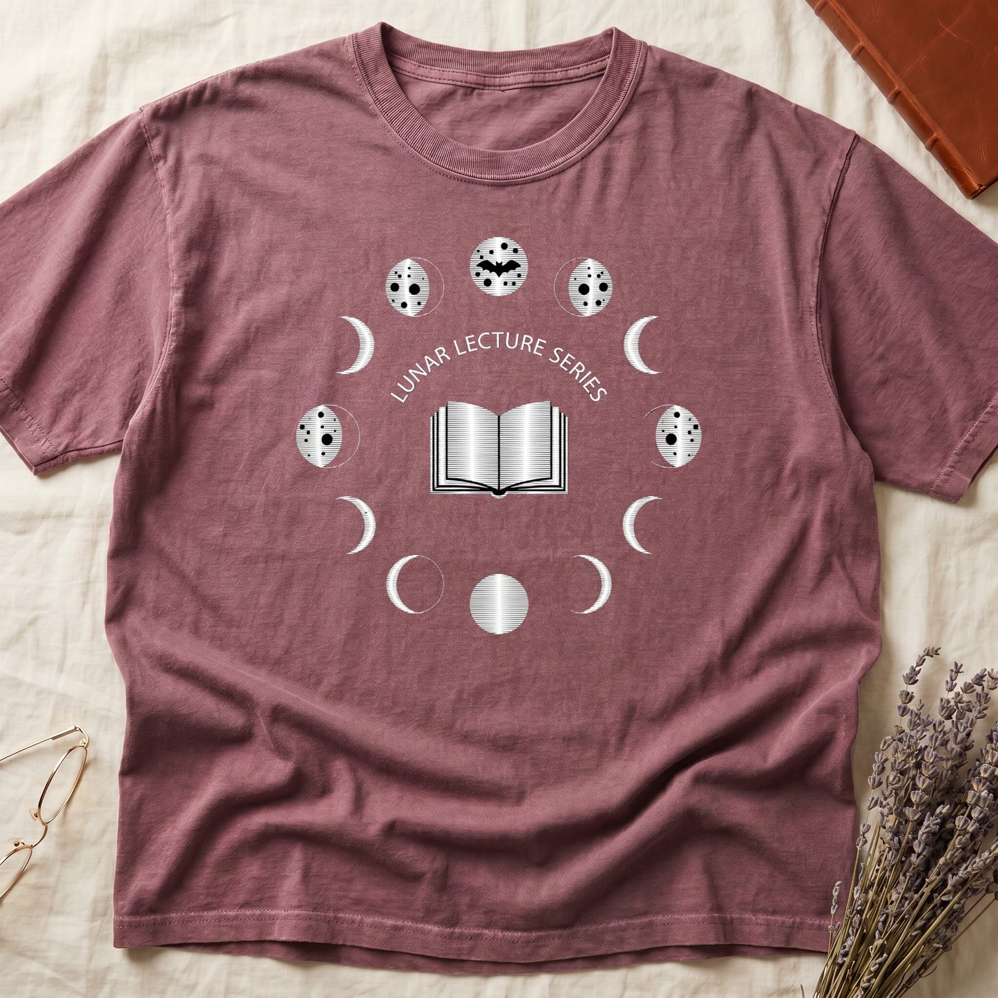 Dark Rose tee with open book at center, ring of cream moon phases around, curved "LUNAR LECTURE SERIES" double-arc above.
