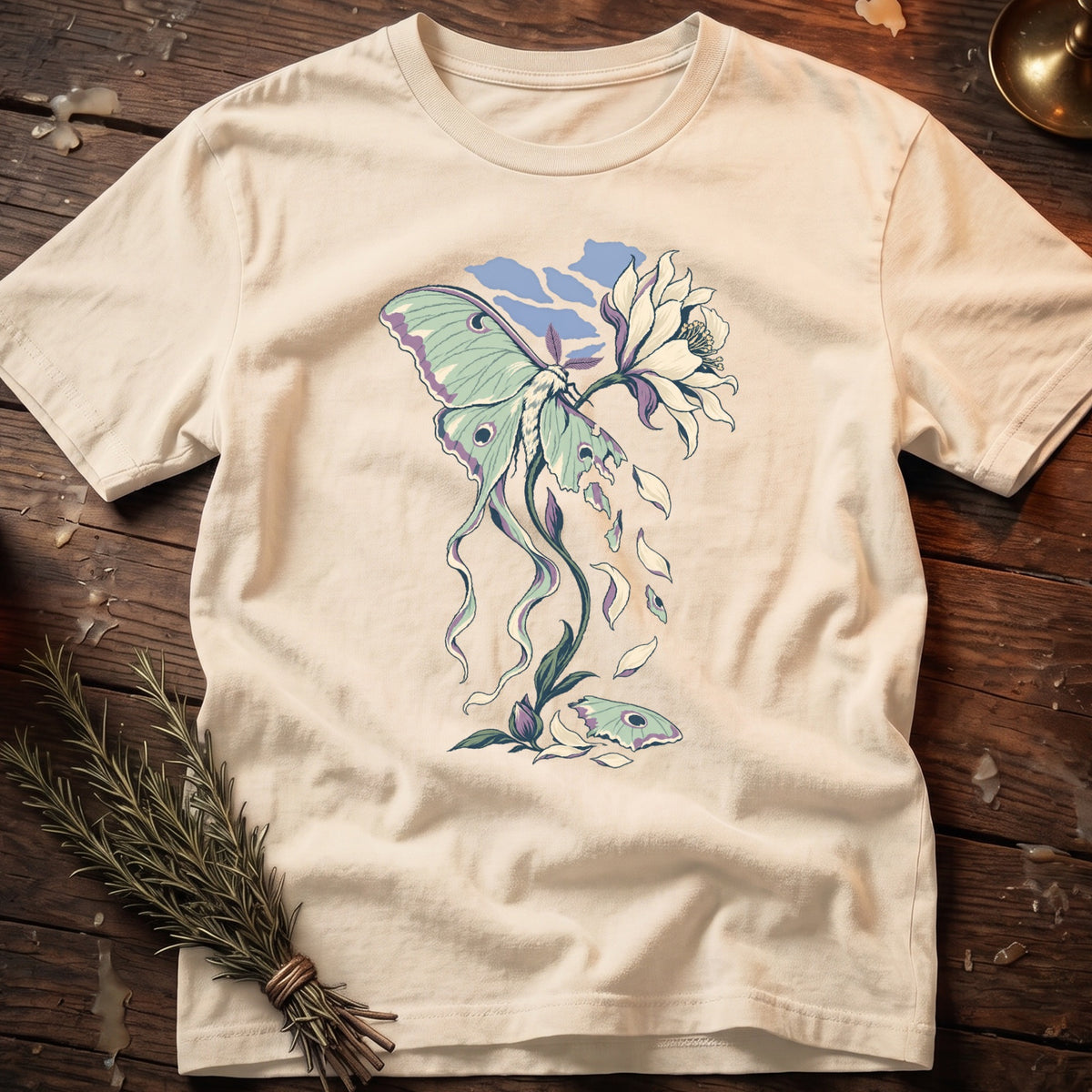 Cream t-shirt with a moth and wilting flower illustration, falling petals, and blue sky.