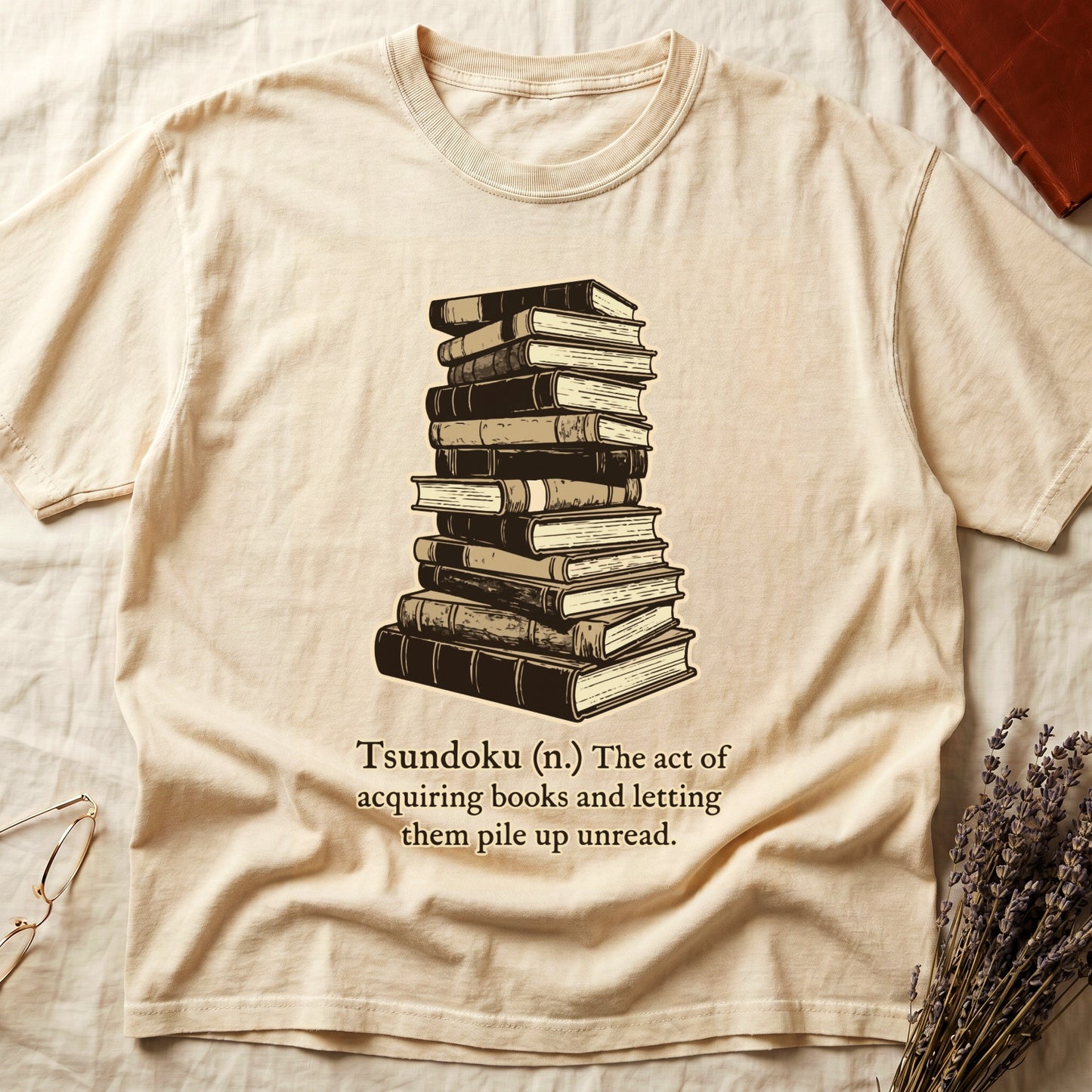 Ivory tee with stack of vintage hardcovers, "Tsundoku (n.) The act of acquiring books and letting them pile up unread."