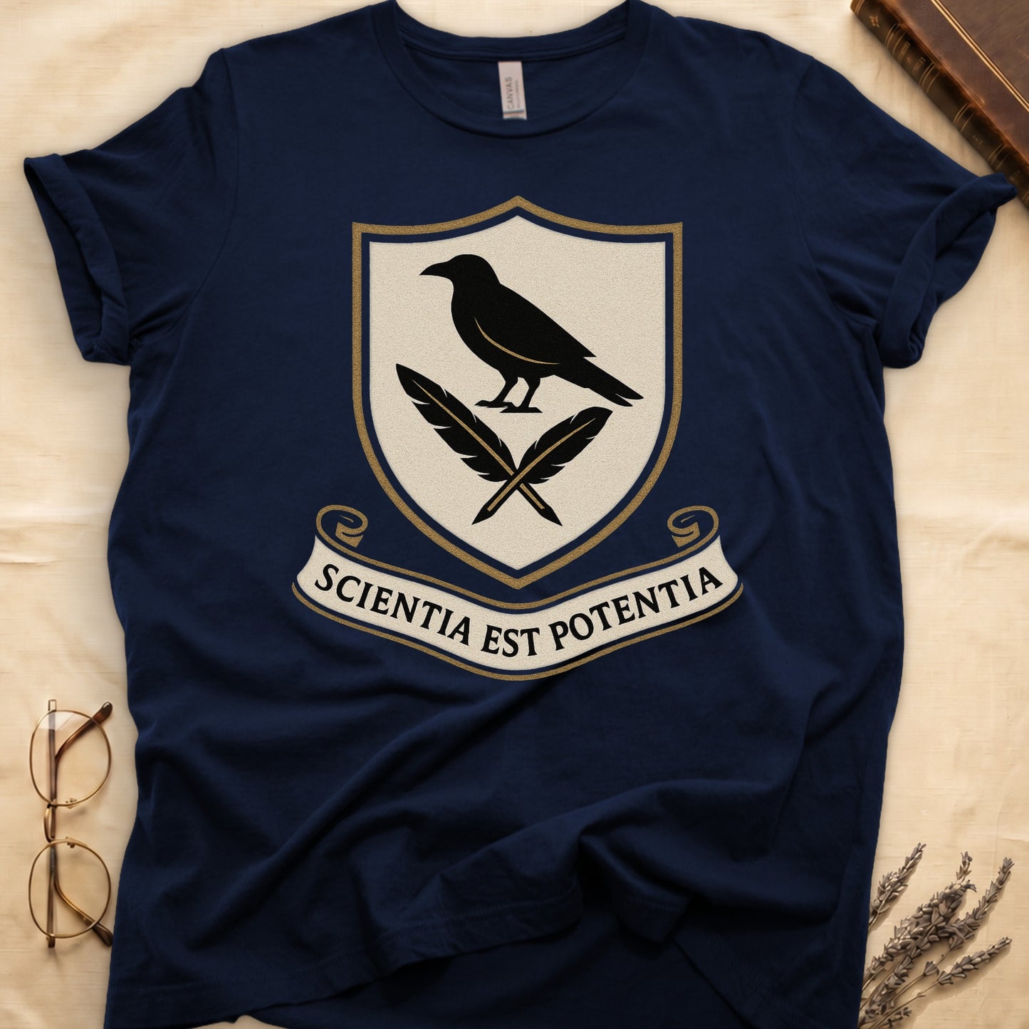Navy tee with cream-and-gold heraldic shield, black raven over crossed quills, scroll banner "SCIENTIA EST POTENTIA" below.