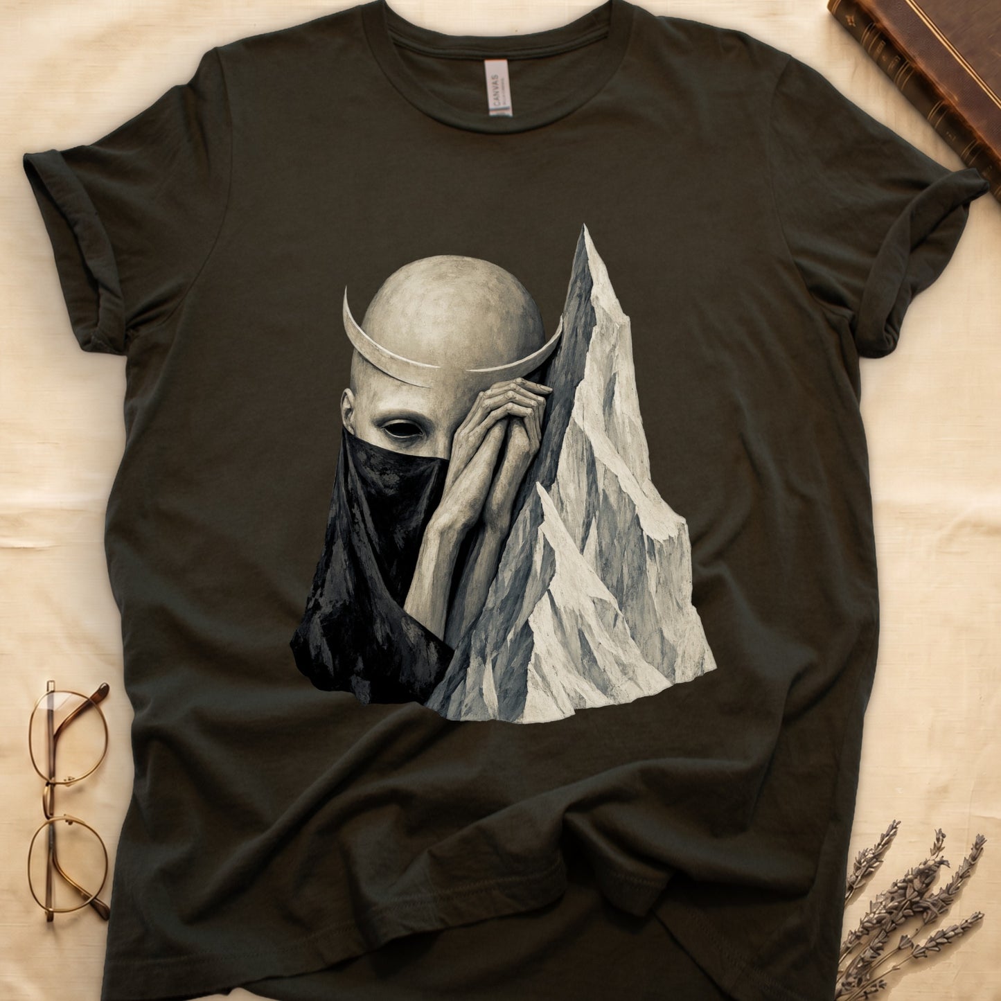 Dark t-shirt with surreal artwork of a bald figure with crescent horns and veiled face by mountains.
