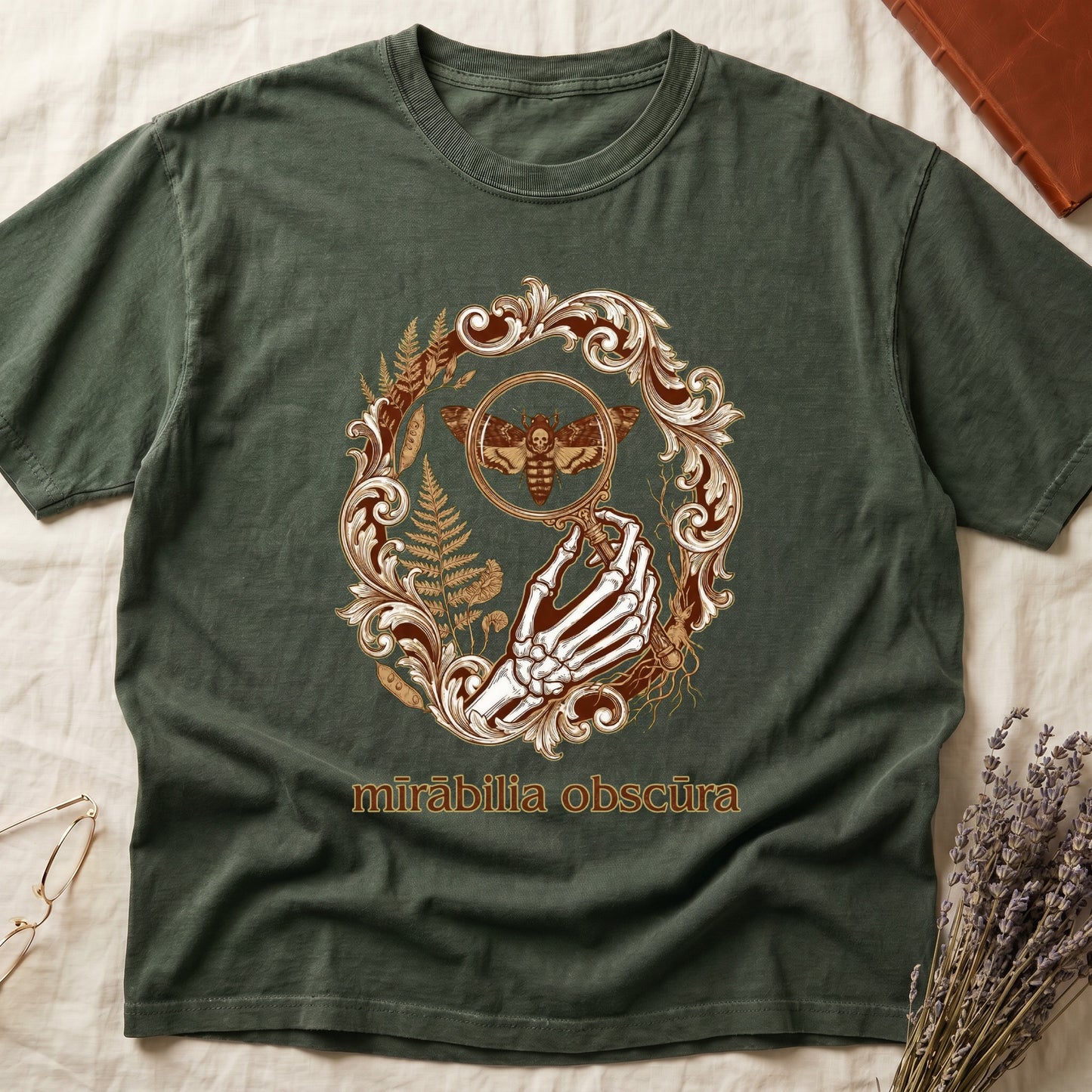 Green tee with skeletal hand, magnifying glass, death's-head moth, ferns on green, "mīrābilia obscūra" in Latin italic.