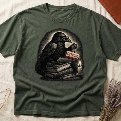 Green tee with bespectacled raven on stacked books, holding wooden "OVERDUE" stamp, lit candle beside, dawn glow behind.