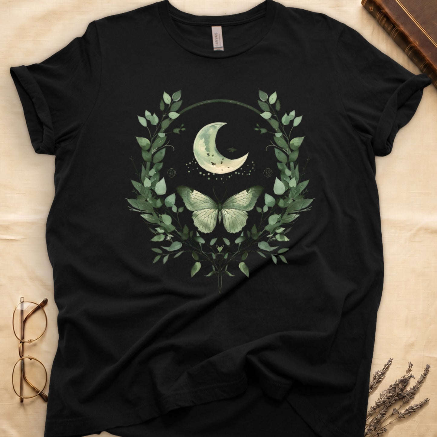 Black t-shirt with a watercolor design of a crescent moon and butterfly within a green leaf wreath.