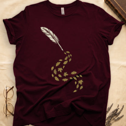 Maroon tee with antique quill pen in cream linework, oak and maple leaves cascading from the nib in gold and green.