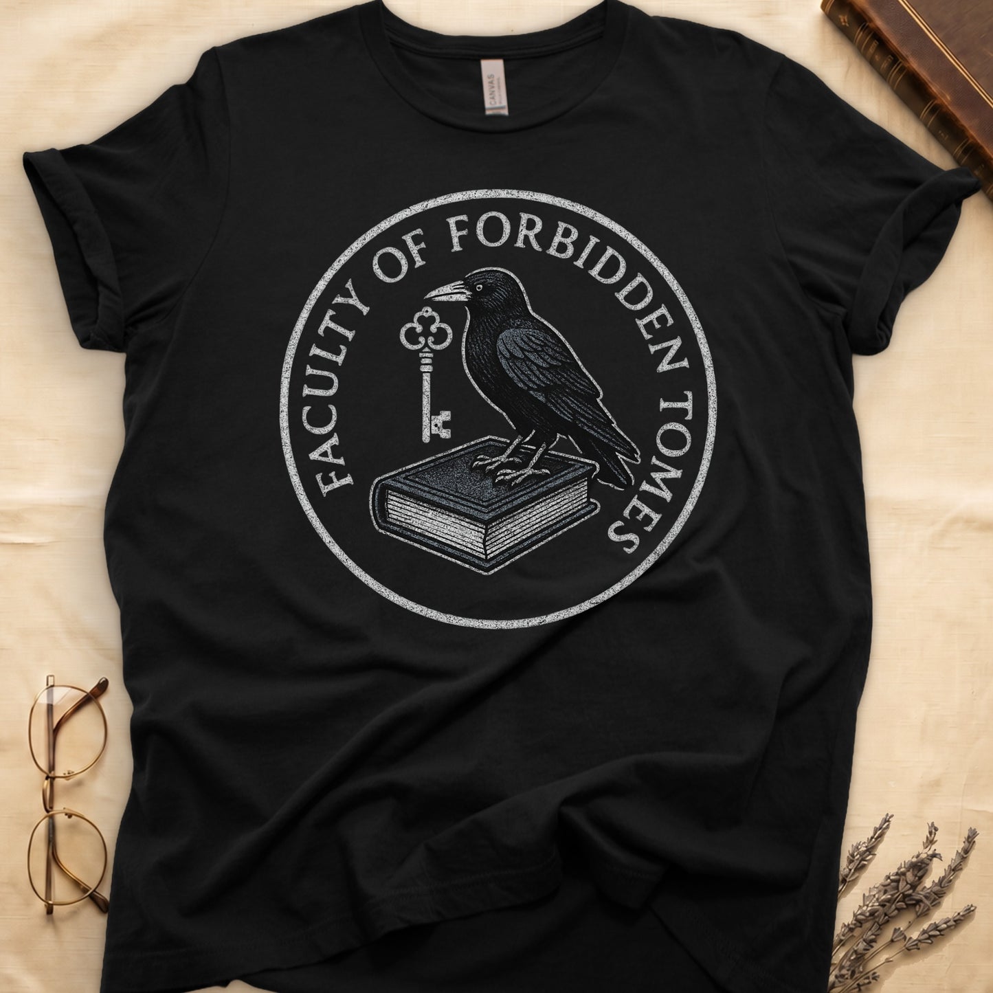 Military Green tee with circular badge, raven on closed book holding key, "FACULTY OF FORBIDDEN TOMES" curved around in cream.