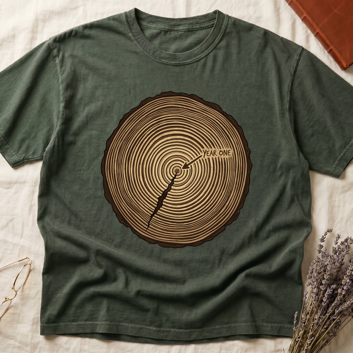 Green tee with cross-section of tree rings in warm brown, arrow pointing to center labeled "YEAR ONE" in serif type.