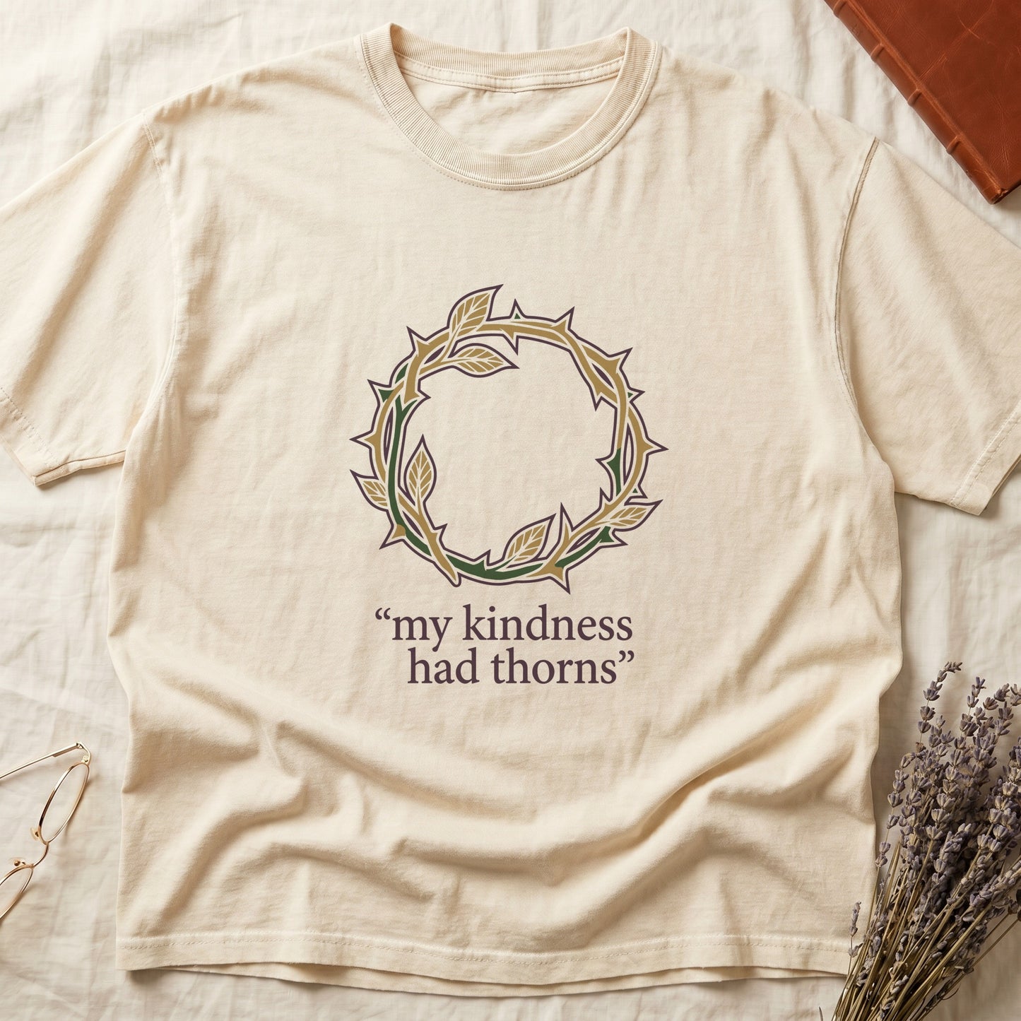 Ivory tee with crown of thorns in gold and red with green leaves, "my kindness had thorns" in cream serif.