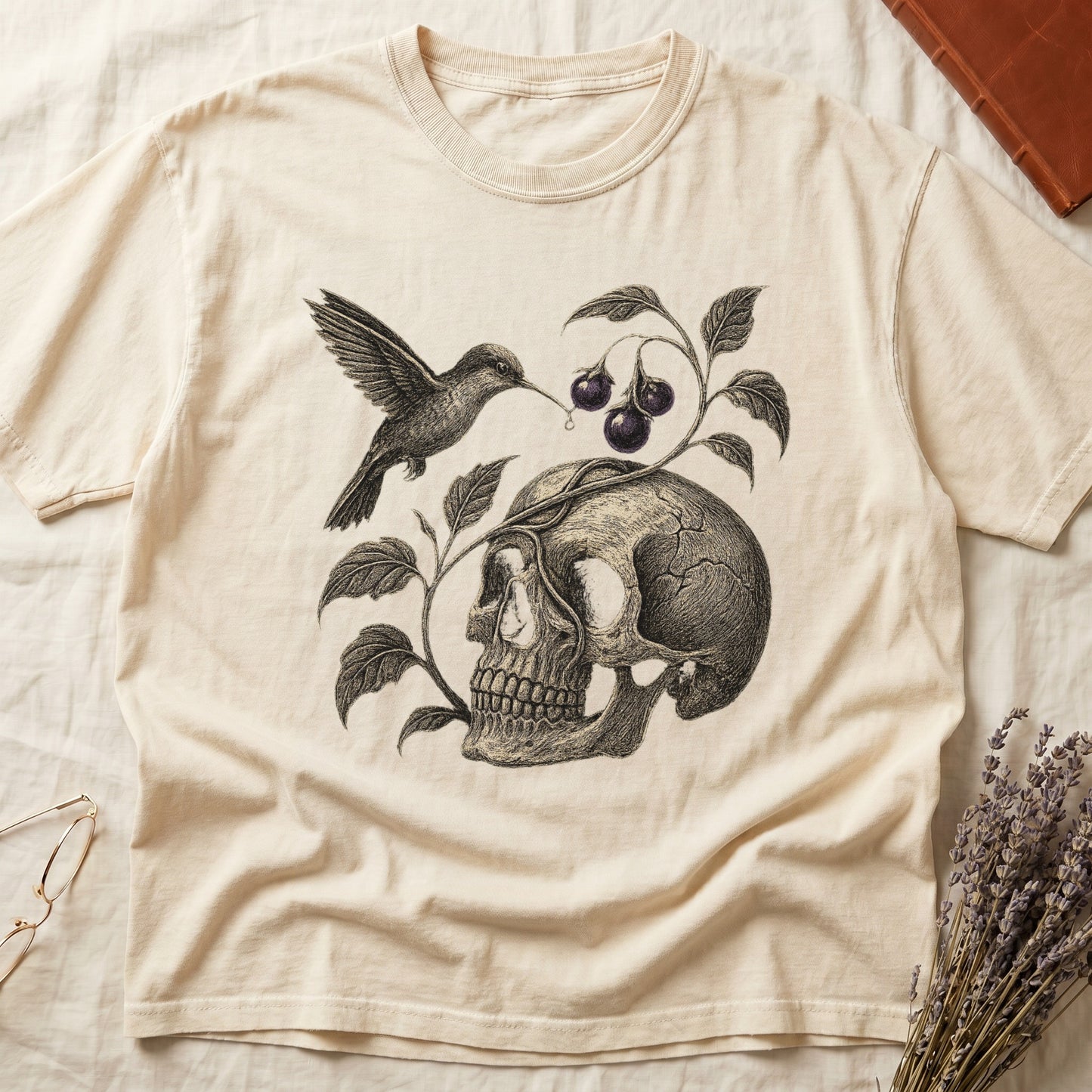 Ivory tee with sepia engraved skull, nightshade vine and dark-purple berries wrapping around, hummingbird at upper left.
