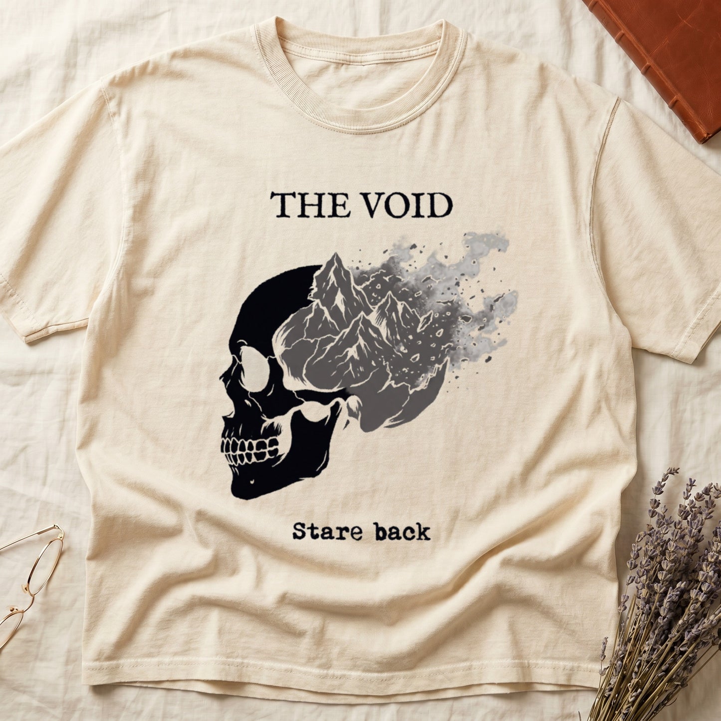 Ivory tee with skull eroding into mountain landscape and stardust, "THE VOID" top, "Stare back" typewriter below.